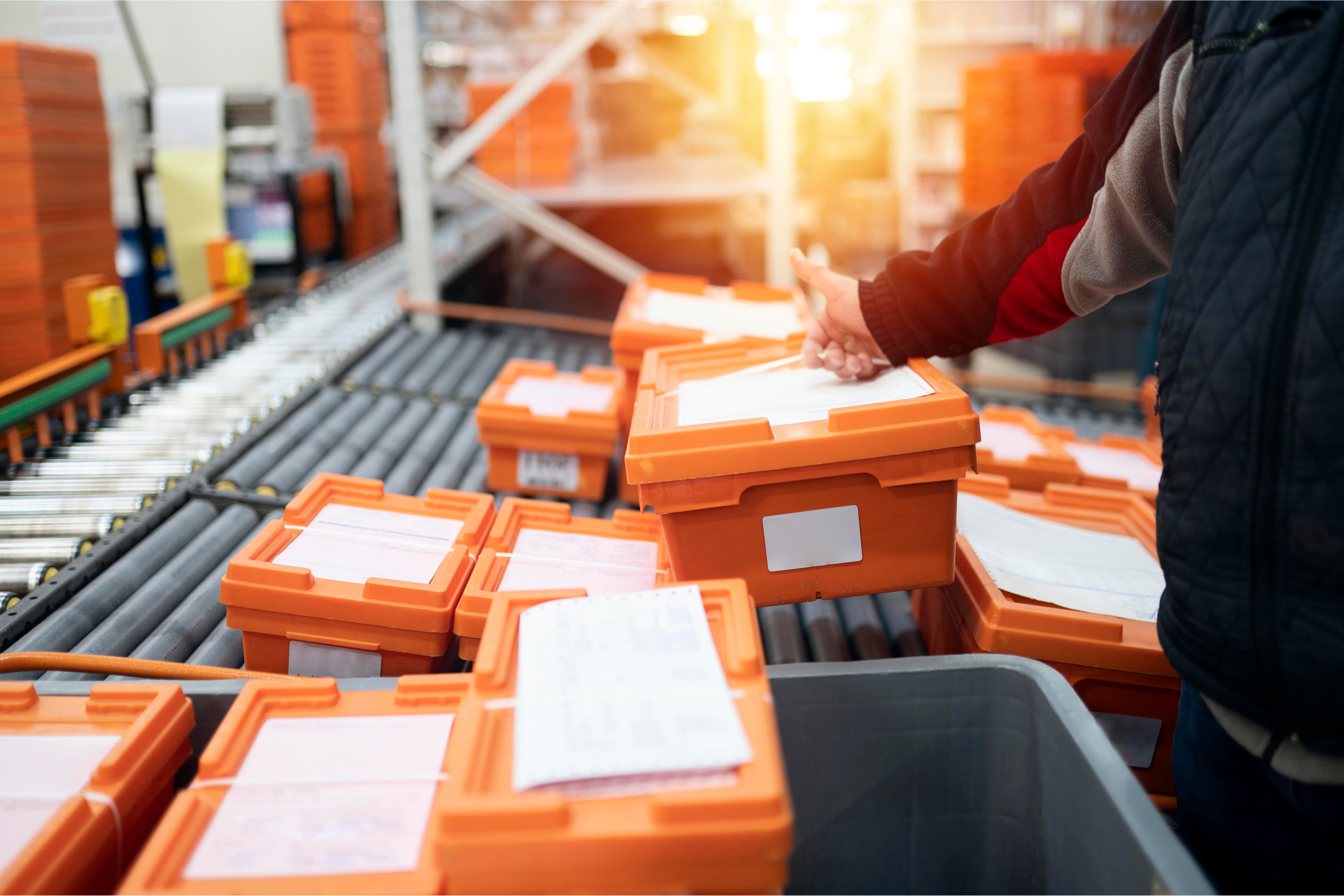 A man grabbing a plastic orange tote off a conveyor belt