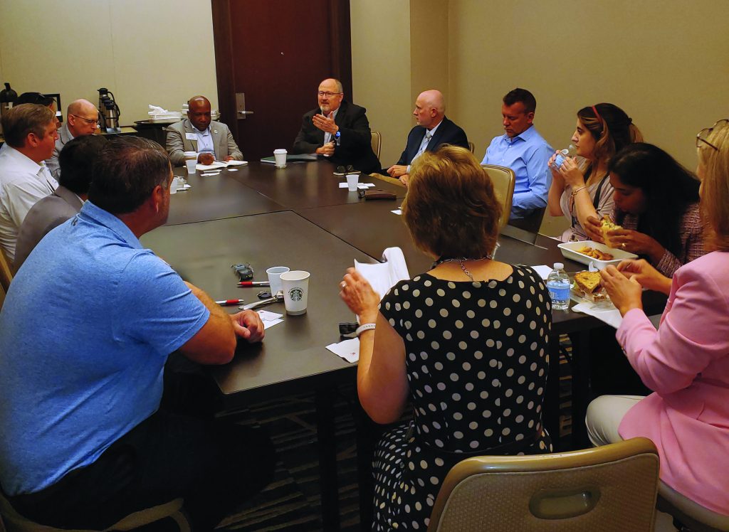 A diverse group of men and women crowded around brown conference room table.